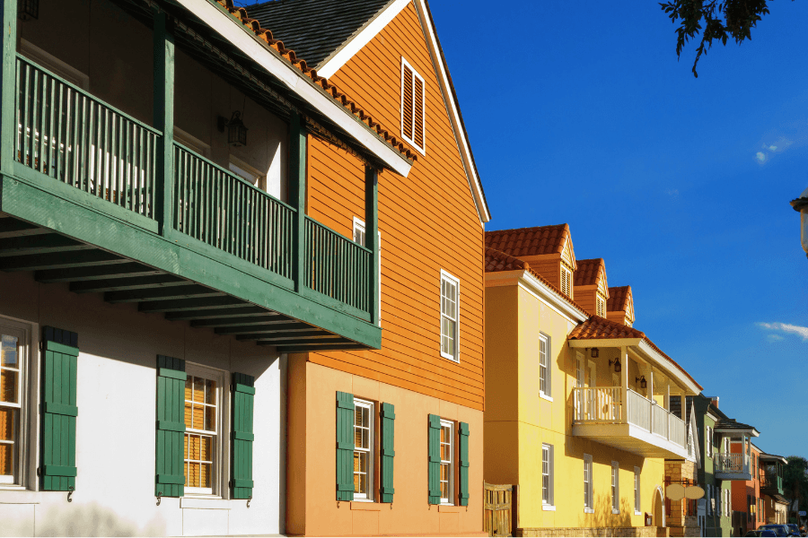 Colorful houses with green shutters and balconies against a blue sky.