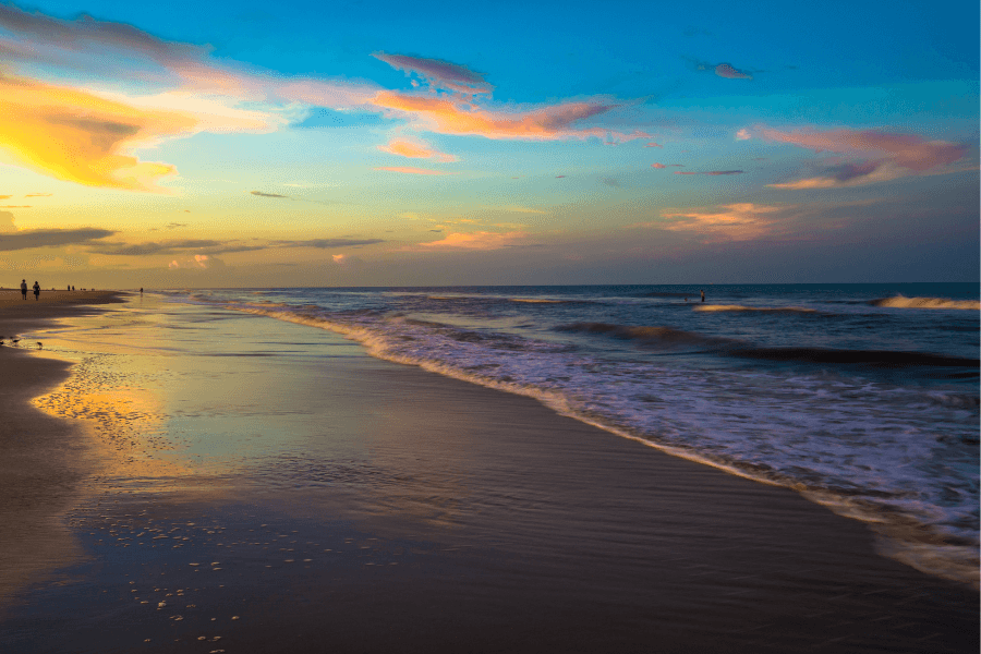 A serene beach at sunset with colorful skies and gentle waves.