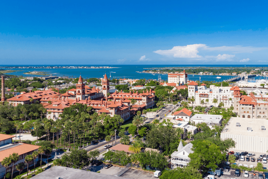 Aerial view of historic buildings and palm trees in St. Augustine, Florida, with the coastline in the background.