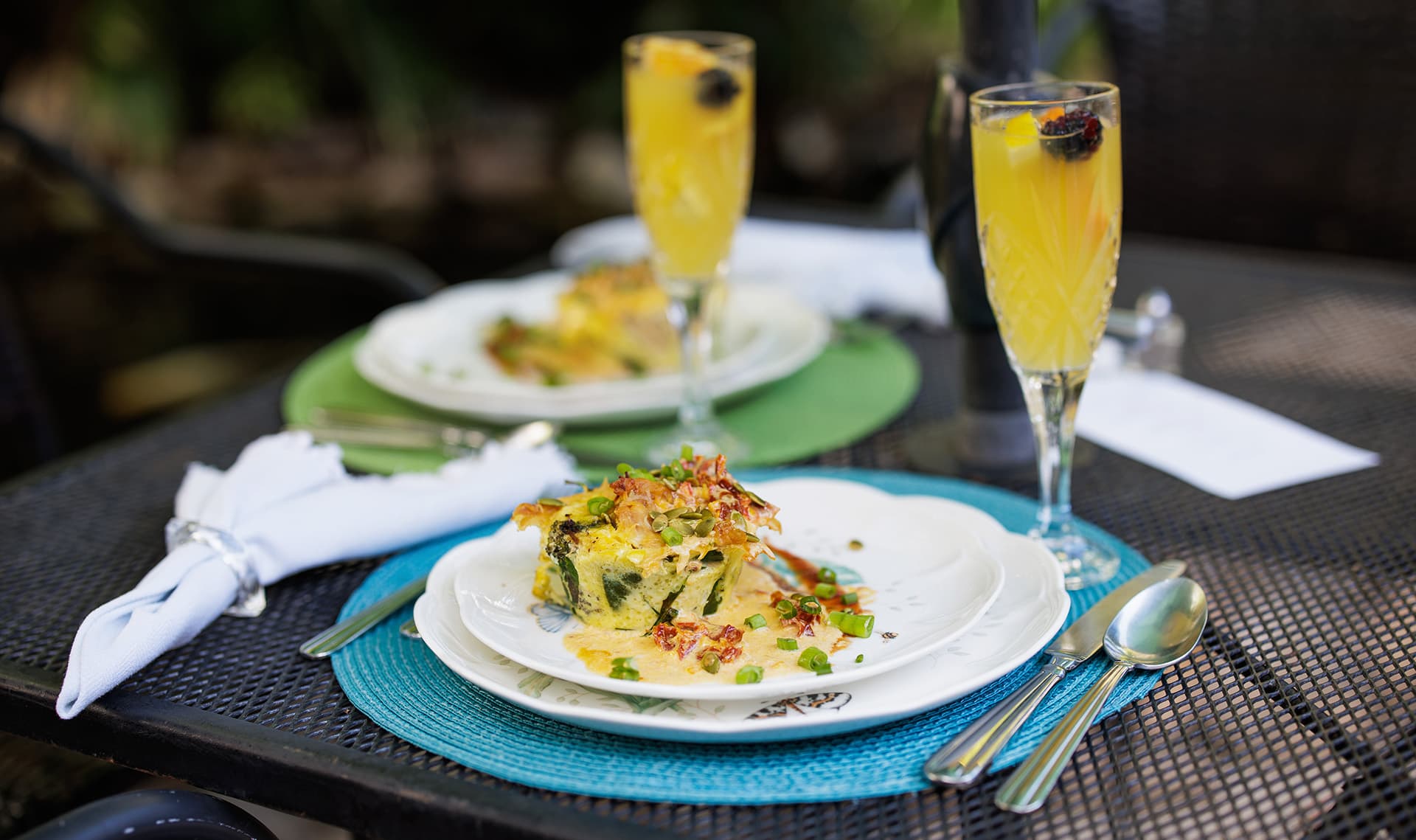 A beautifully arranged brunch setting featuring a plate of frittata and two glasses of mimosa.