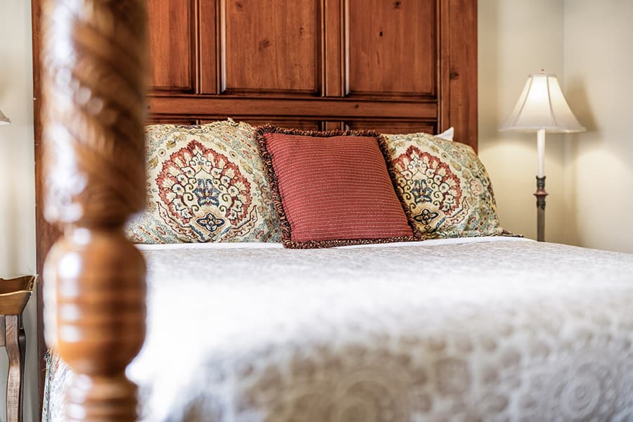 A stylish bed with ornate pillows and a warm wooden headboard, accompanied by a bedside lamp.