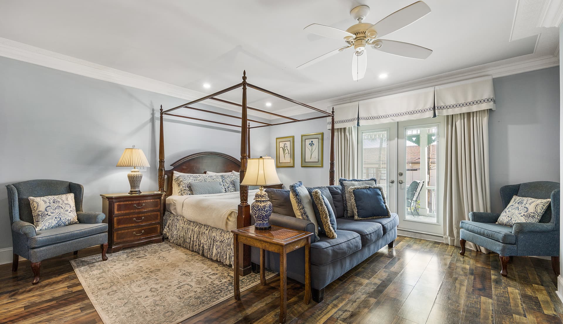 A stylish bedroom featuring a four-poster bed, plush seating, and natural light from double doors.