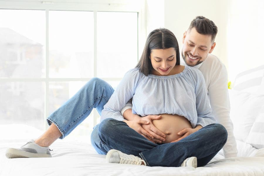 A happy couple shares an intimate moment as the man gently holds the woman's pregnant belly.