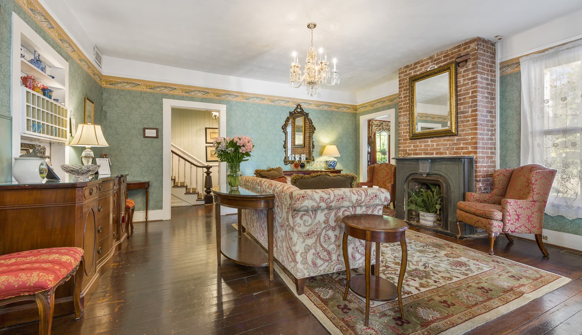 A cozy living room featuring vintage furnishings, a fireplace, and decorative wallpaper.