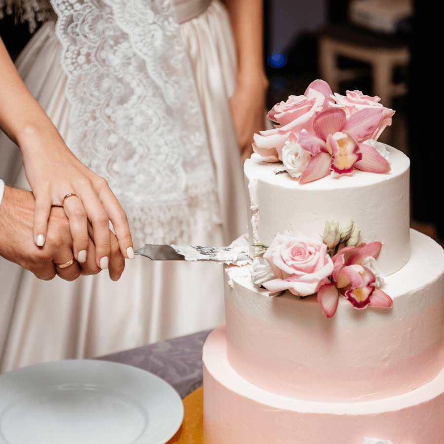 A couple prepares to cut a wedding cake adorned with pink flowers.