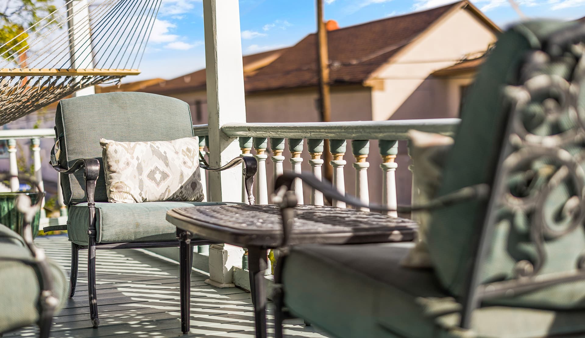 A cozy porch featuring two green chairs and a small table with a pillow on one chair.