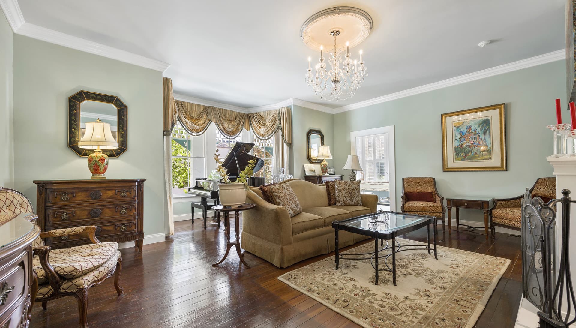 A stylish living room featuring a sofa, decorative furniture, and a grand piano under a chandelier.