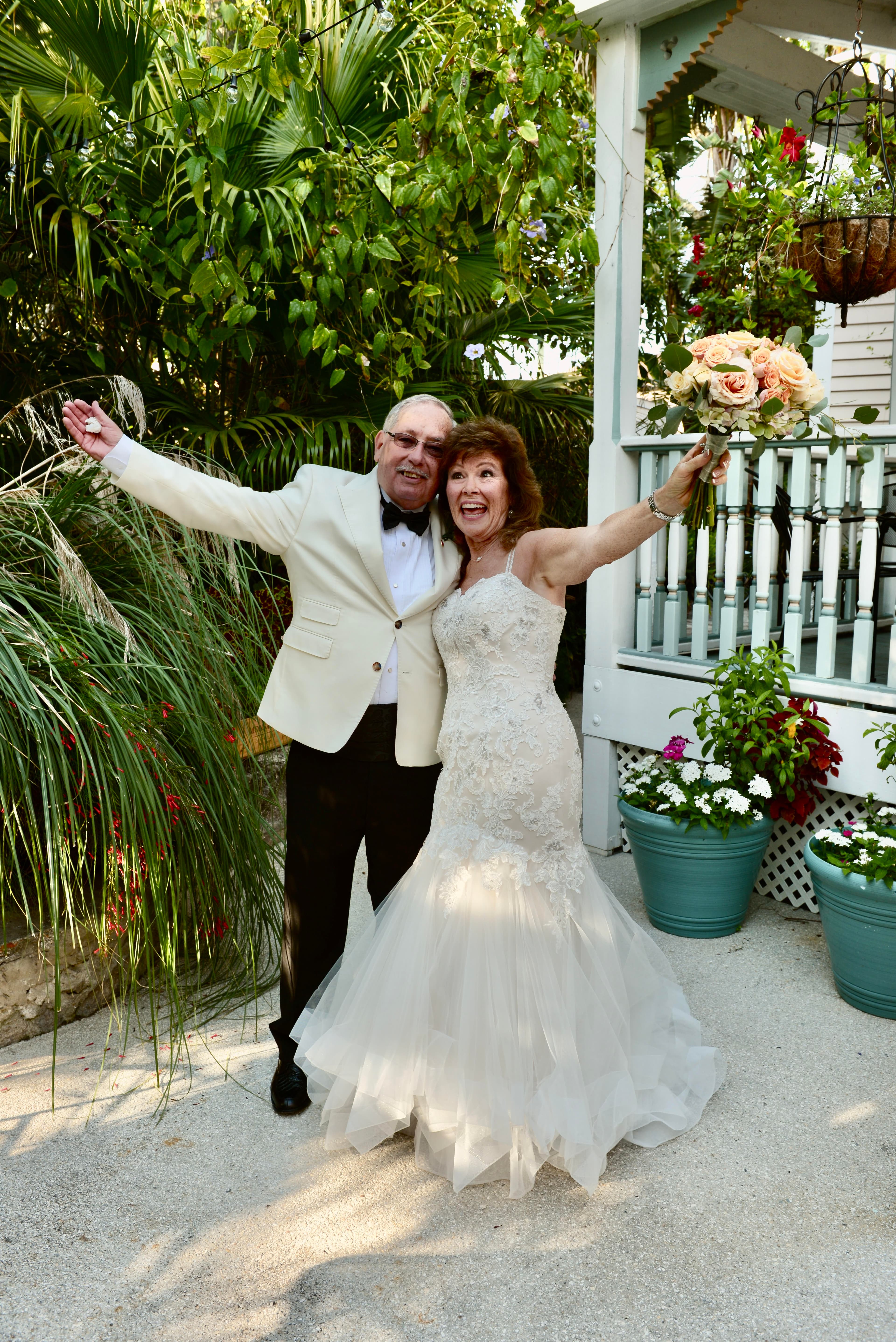 A jubilant couple celebrates their wedding outdoors amid lush greenery and floral arrangements.